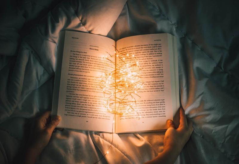 Photo of a person holding string lights on an opened book.