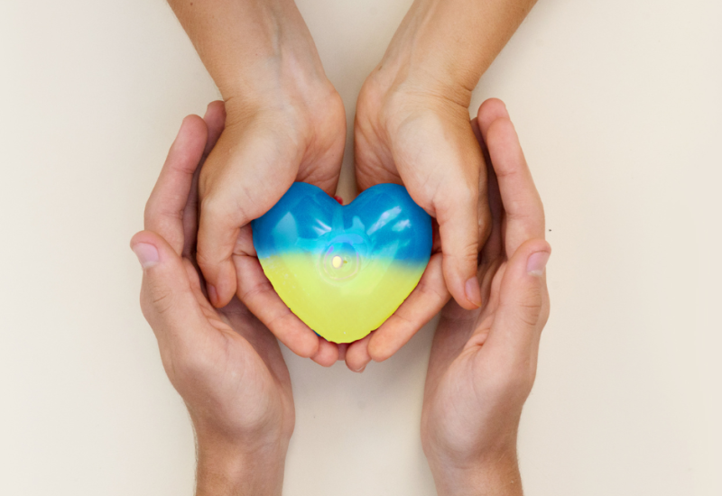 A heart in the colours of the Ukrainian flag held by two pairs of hands.