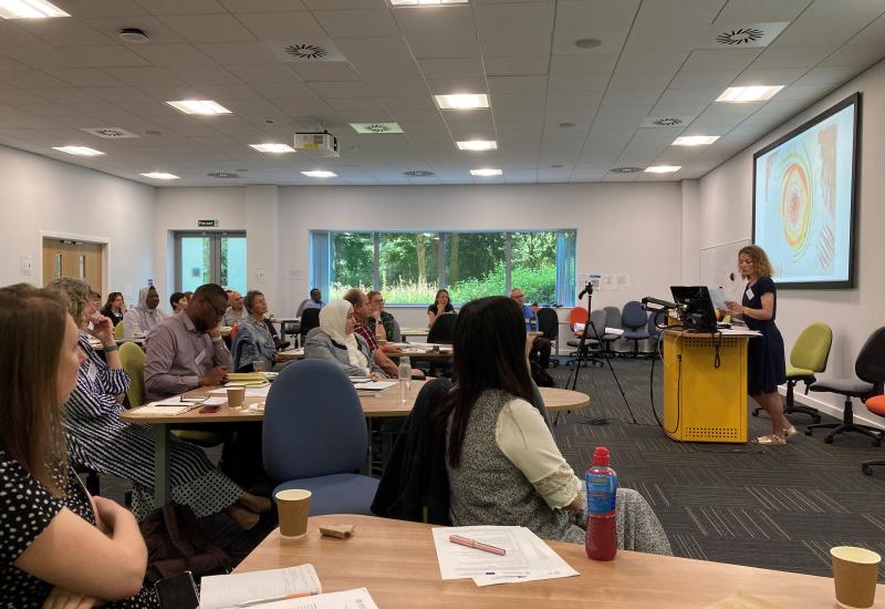 People sitting at tables listening to a speaker giving a presentation.