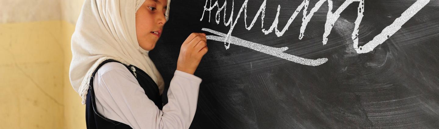 A young girl writing the word asylum on a chalk board
