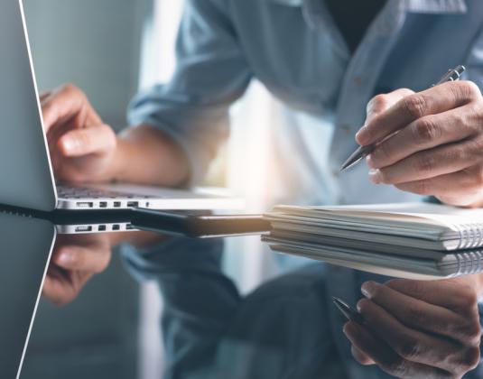 A person working on a laptop and making notes