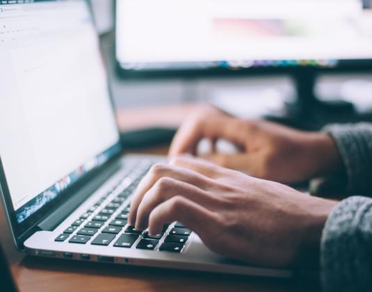 Photo of two hands typing on a laptop keyboard