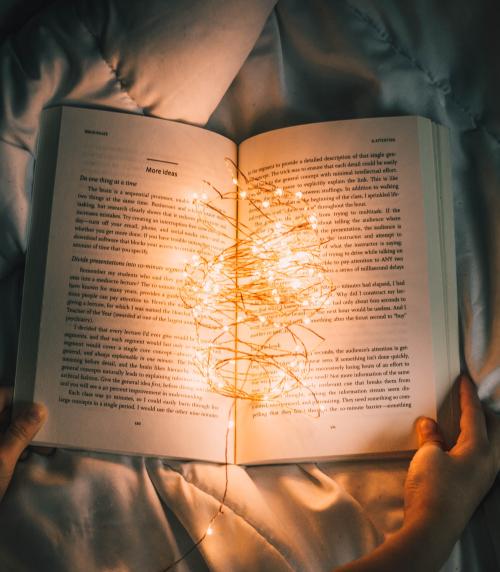 Photo of a person holding string lights on an opened book.