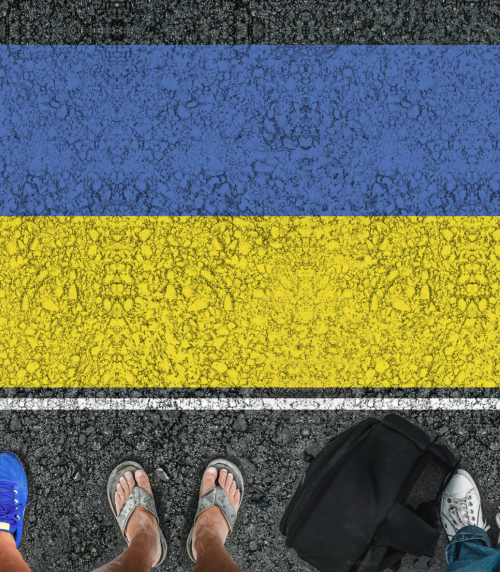 People's legs standing on asphalt road on which the flag of Ukraine is drawn.