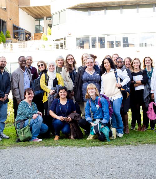 Photo of a group of about 25 people, standing or sitting on grass in front of a modern building.